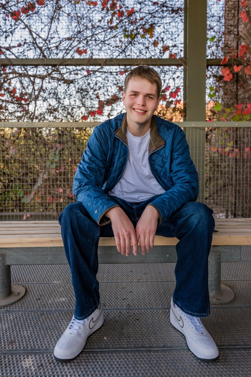 Logan Parker smiling, seated on a bench with fall foliage behind him
